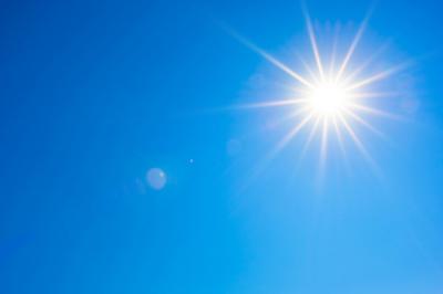 Bright sun shining in a clear blue sky with light sun rays extending outward and a few small lens flares visible.
