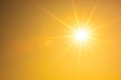 Bright sun shining in a clear yellow-orange sky with visible rays spreading outward, creating a warm and glowing atmosphere.